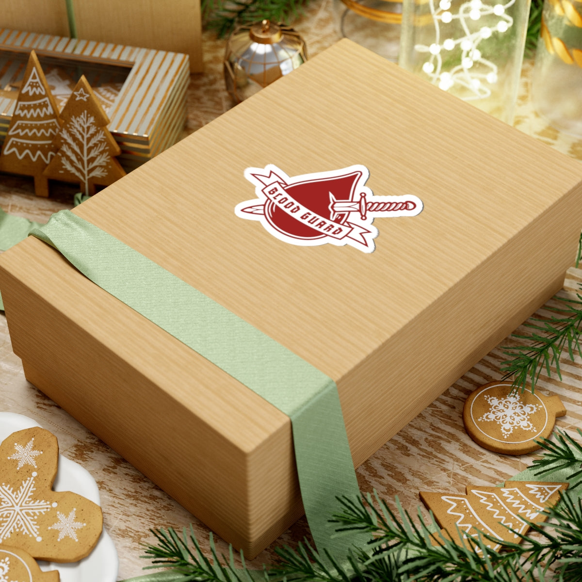 Sticker from thtgrlreads featuring the Bloodwing Academy collection, displaying a red crest with a sword and "Blood Guard" text on a wrapped gift box surrounded by festive holiday decorations.
