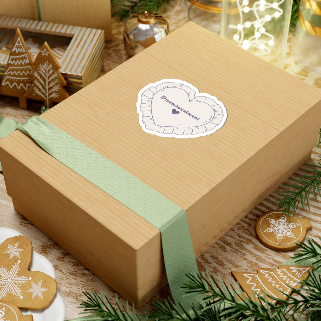 A close-up of a kraft gift box tied with a soft green ribbon featuring a thtgrlreads Disembowelment embroidery sticker from The Poison Daughter collection, surrounded by festive gingerbread cookies and holiday decor.
