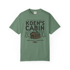 Green Comfort Colors graphic tee featuring Koen's Cabin lettering, a woodland cabin, pine trees, and Northwest Territory text from Thtgrlreads in Tees and Ali Hazelwood