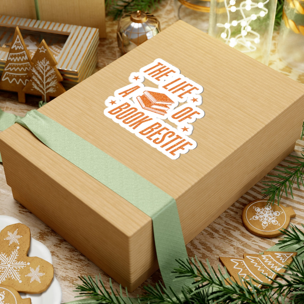 A "Life of a Book Bestie" sticker from thtgrlreads, part of the Stickers and The Life of a Book Bestie collections, featuring orange lettering and book graphics on a kraft paper gift box with a sage green ribbon.