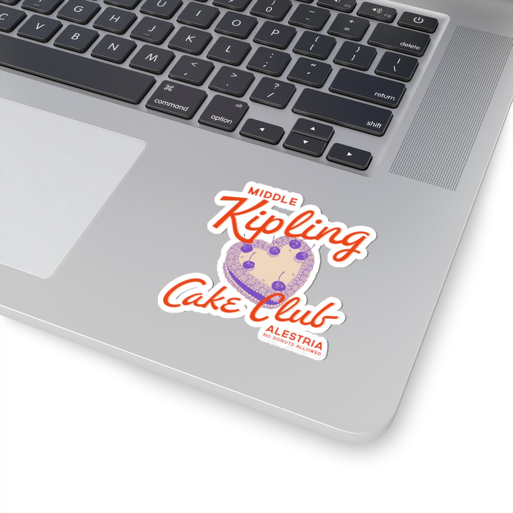 Sticker from thtgrlreads' Ruthless Boys of the Zodiac collection featuring a whimsical design with orange script text "Middle Kipling Cake Club" above a purple cake illustration, placed on a silver laptop.