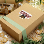 A Bloodwing Academy Crest Sticker from the thtgrlreads Back to School and Bloodwing Academy collections displayed on a brown gift box with a light green ribbon, surrounded by festive gingerbread cookies and holiday decor.
