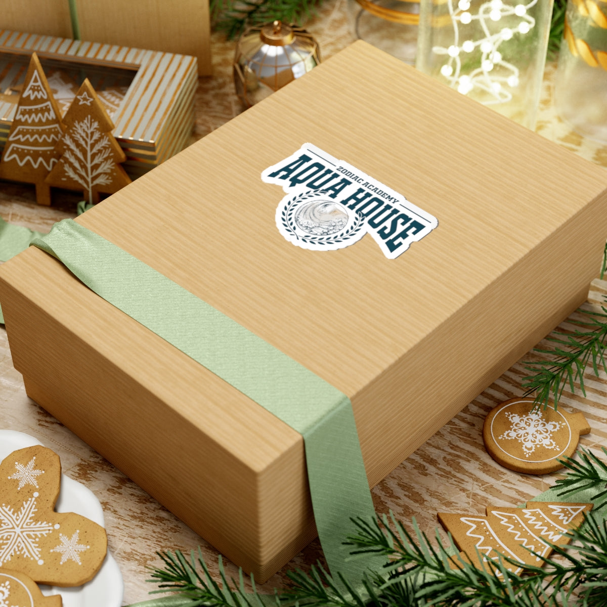 A Zodiac Academy themed Aqua House sticker from thtgrlreads displayed on a gift box wrapped with a green ribbon, surrounded by festive gingerbread cookies and holiday decor.