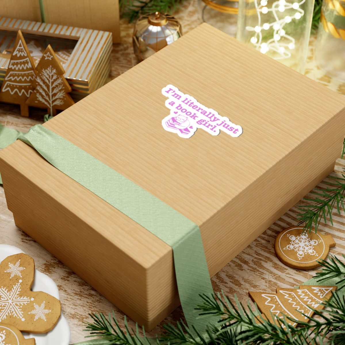 Brown gift box wrapped with a light green ribbon featuring a "I'm literally just a book girl" sticker from thtgrlreads, surrounded by festive gingerbread cookies and holiday decorations.