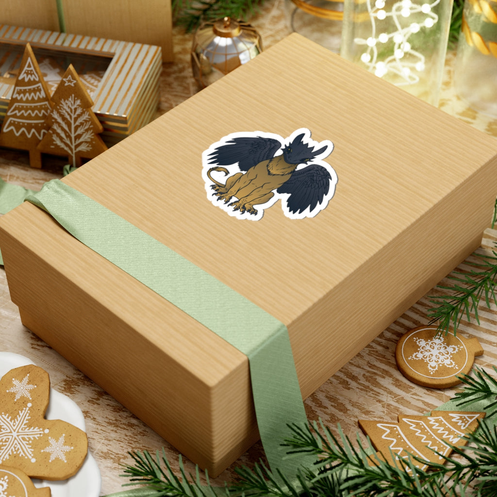 A fantasy-inspired sticker from thtgrlreads featuring a winged creature design, part of the Kindred's Curse Saga sticker collection, placed on a gift box with festive decor.