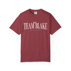 Bloodwing Academy Comfort Colors graphic tee by thtgrlreads in vintage wash maroon with white "Team Blake" text and a small flying bird graphic, part of official romance fandom merch.
