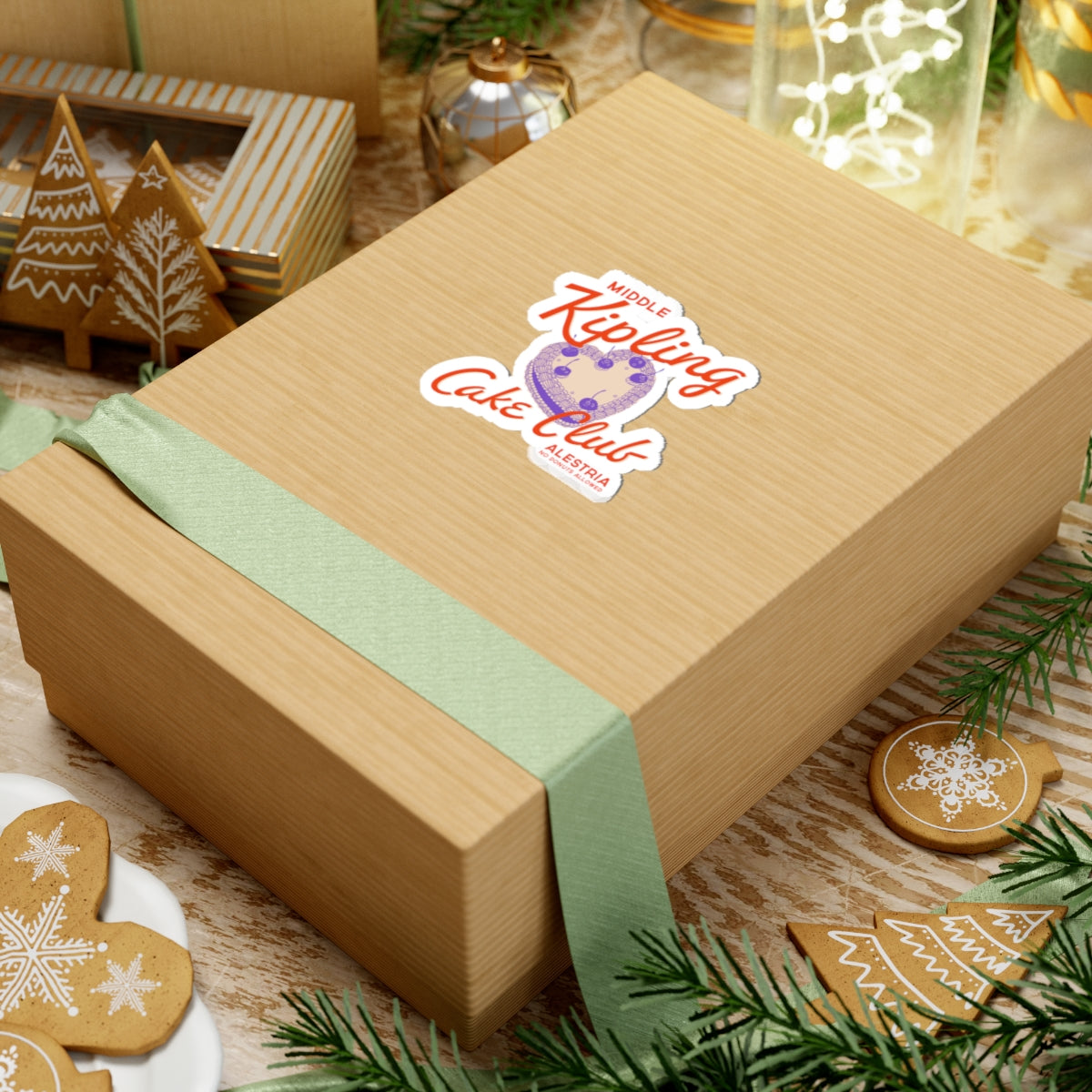 Thtgrlreads Ruthless Boys of the Zodiac collection sticker featuring a vintage-style cake club graphic on a kraft gift box with festive holiday decor and green ribbon accents.