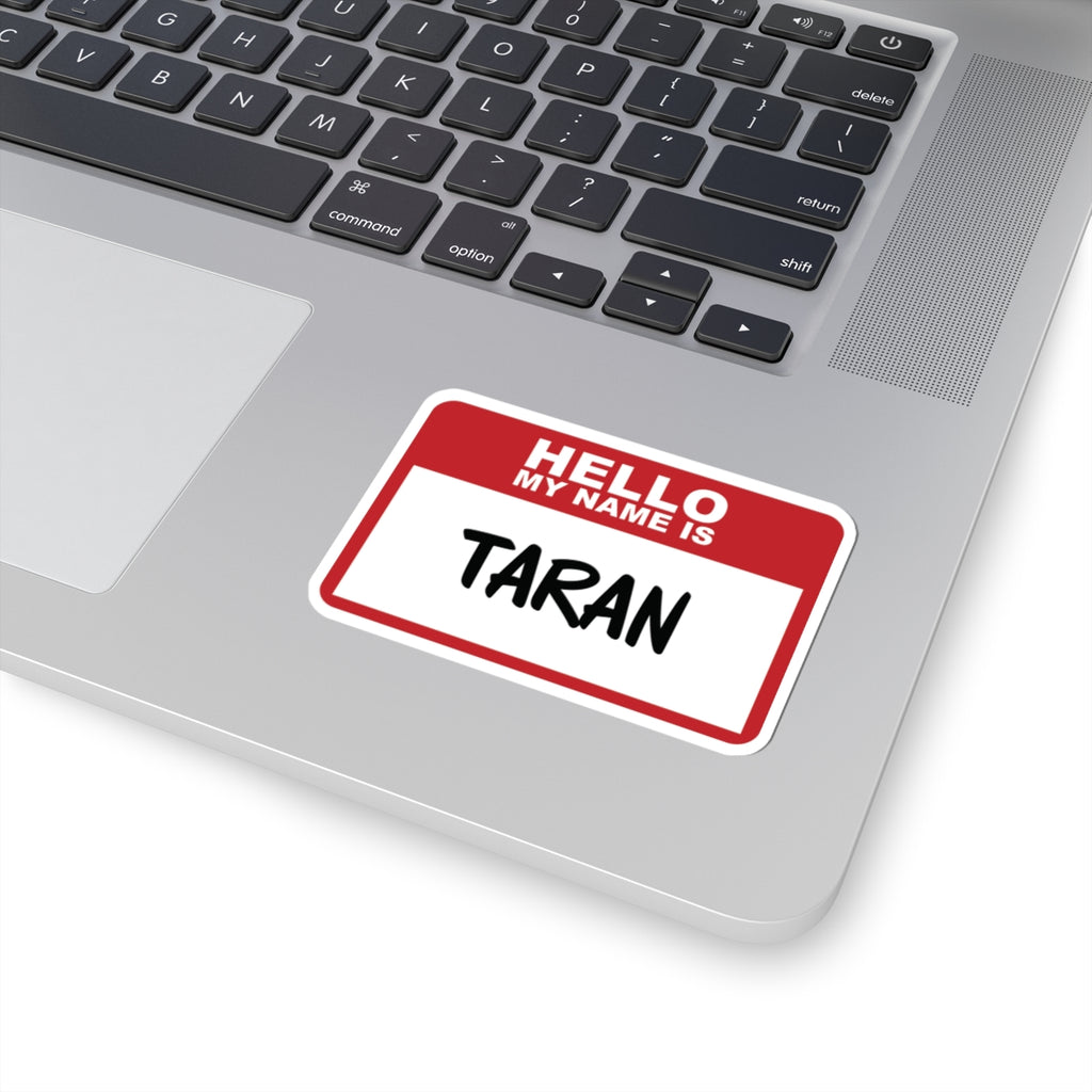Sticker from the Kindred's Curse Saga collection by thtgrlreads featuring a red and white "Hello My Name Is" design with the handwritten name Taran, placed on a laptop surface.
