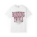 A white Comfort Colors graphic tee from thtgrlreads featuring vintage wash fabric and bold maroon "The Bonding Trials" text with an illustrated wolf design, part of Wolves of Ruin and Tees collections.