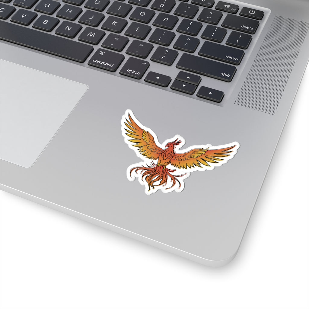 A vibrant phoenix sticker from the Kindred's Curse Saga collection by thtgrlreads, featuring fiery orange and yellow wings on a white laptop surface.