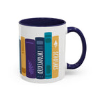 A white ceramic mug with a navy blue handle and interior, featuring a colorful graphic of vertically standing books with titles like "INTROVERTED" and "SCHOLARS" in a playful, minimalist design.