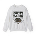 Light gray Koen's Cabin crewneck sweatshirt featuring a mountain cabin and pine trees from Thtgrlreads Ali Hazelwood collection