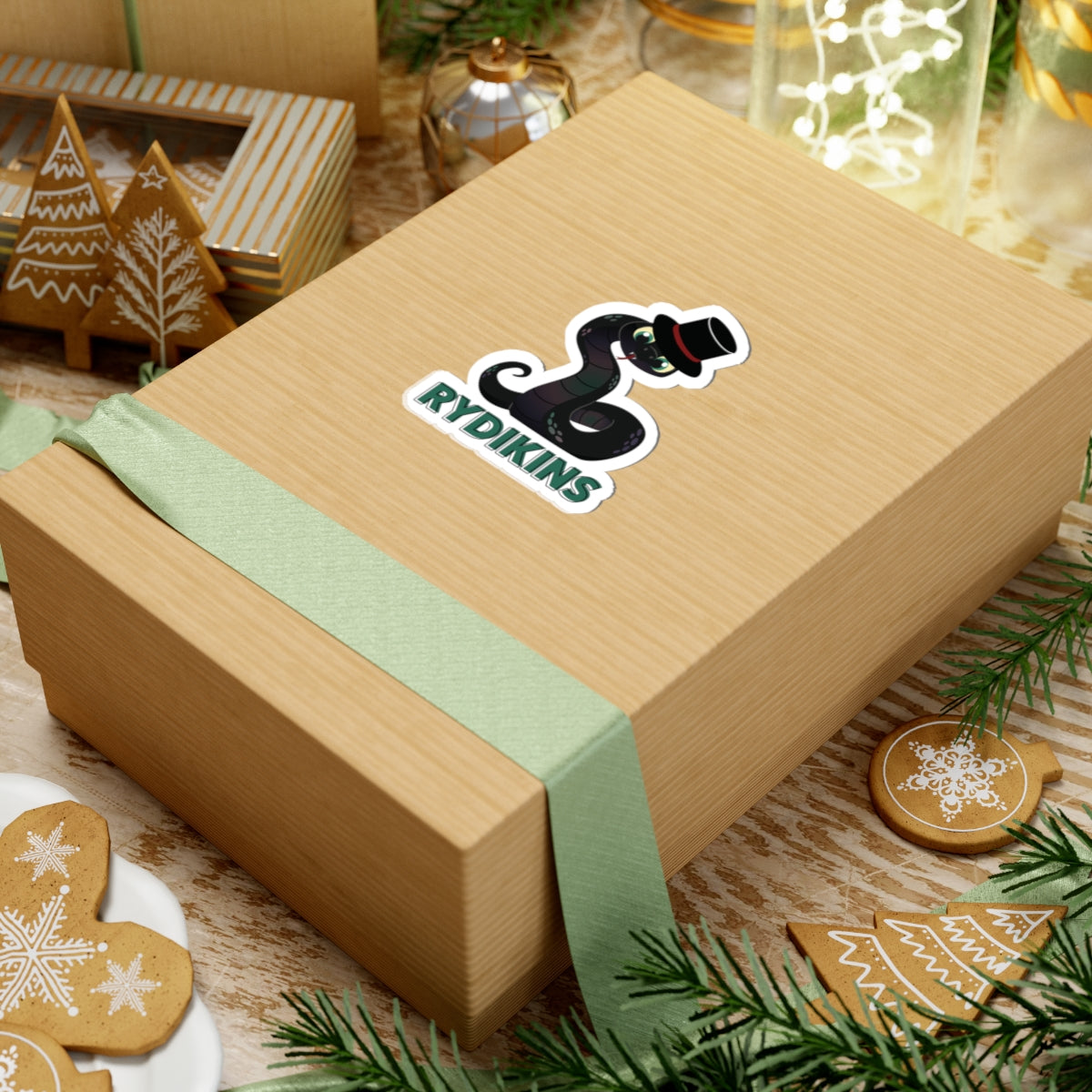 A Rydikins sticker from the Ruthless Boys of the Zodiac collection by thtgrlreads, featuring a black snake with bright eyes and a top hat on a gift box with green ribbon.