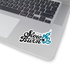 A close-up of a silver laptop keyboard area with a "Slow Burn Club" sticker featuring black cursive text and a blue flame graphic near the touchpad.