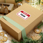 Thtgrlreads Kindred's Curse Saga sticker featuring a classic red and white nametag design with "Taran" in bold black text, shown on a gift box amidst festive holiday decorations.