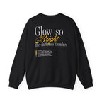 A black Comfort Colors crewneck sweatshirt from thtgrlreads featuring a typographic design with the phrase "Glow so Bright the darkness trembles" in white and orange script fonts on the back.